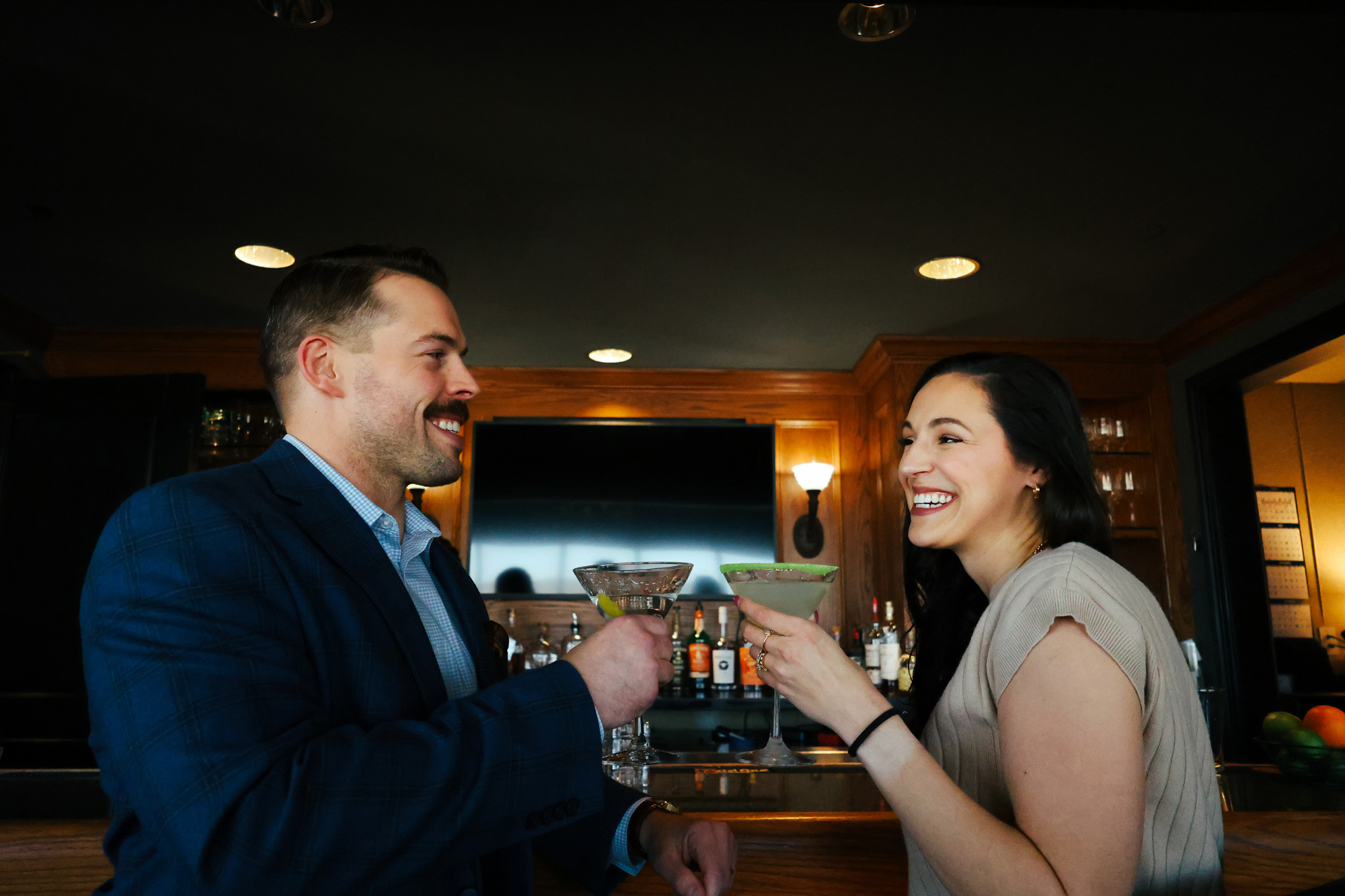 A couple toasting their glasses in front of the bar in the Tavern at The Walden Club.
